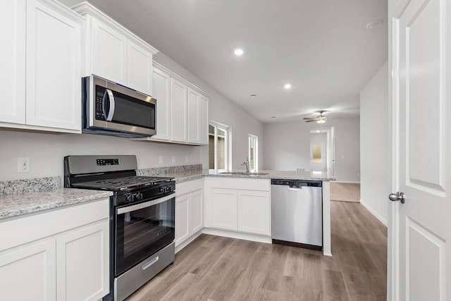 kitchen with a peninsula, stainless steel appliances, light wood-style floors, white cabinetry, and a sink