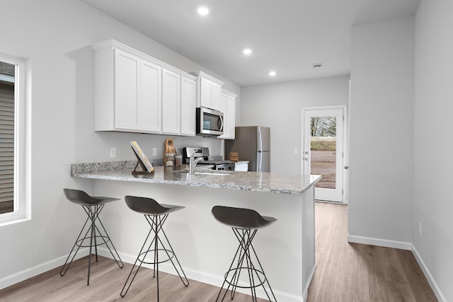 kitchen with light wood finished floors, appliances with stainless steel finishes, a kitchen breakfast bar, a peninsula, and recessed lighting