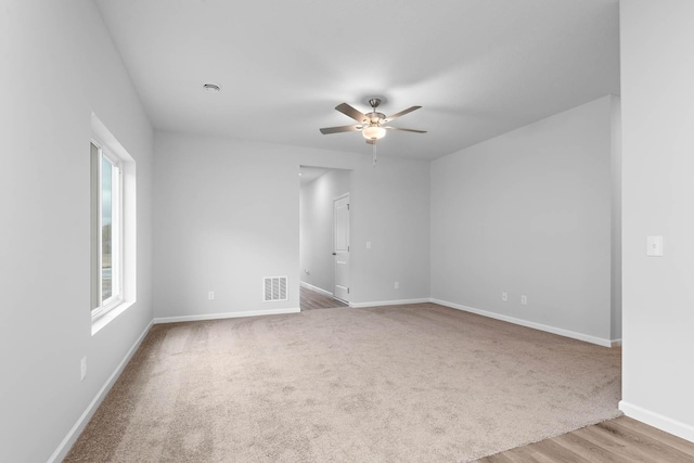 spare room with wood finished floors, a ceiling fan, visible vents, and baseboards