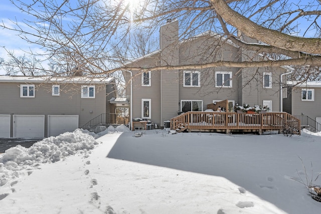 snow covered house featuring a garage, a wooden deck, and a chimney