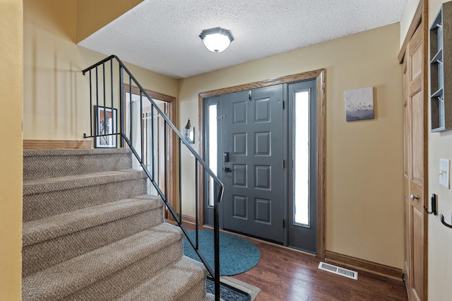 foyer entrance featuring baseboards, wood finished floors, visible vents, and a textured ceiling