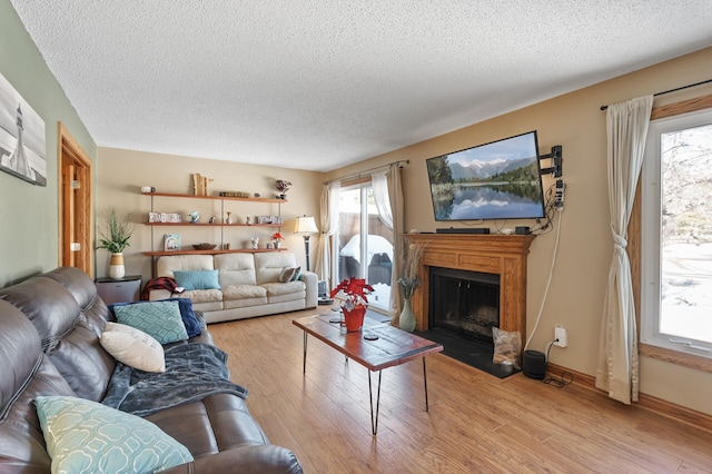 living room featuring a fireplace with flush hearth, light wood-style flooring, a textured ceiling, and baseboards