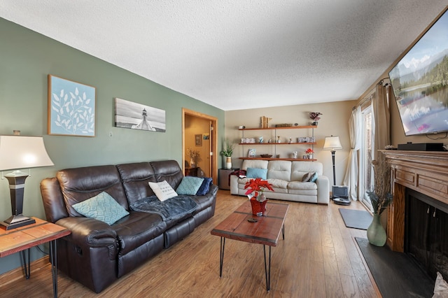 living area with a fireplace with raised hearth, a textured ceiling, and wood finished floors