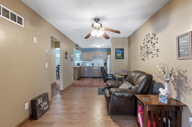 living area featuring visible vents, baseboards, wood finished floors, a textured ceiling, and a ceiling fan