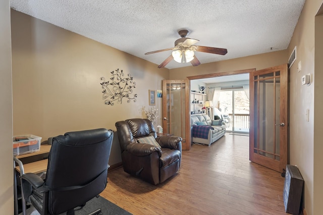 office featuring visible vents, a textured ceiling, light wood-style flooring, and a ceiling fan