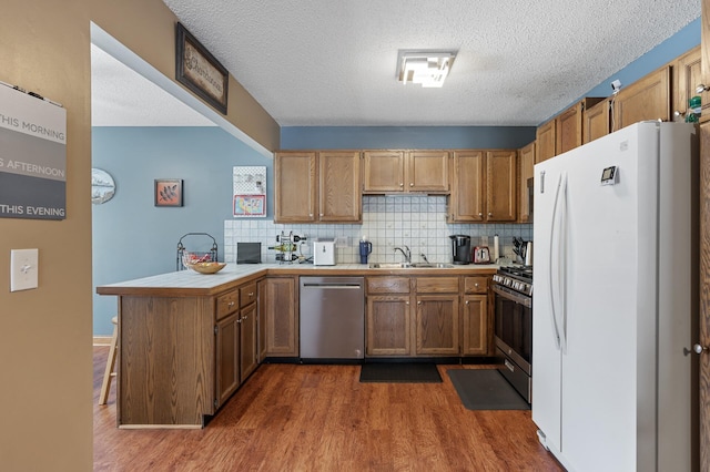 kitchen with dark wood-type flooring, tasteful backsplash, stainless steel appliances, a peninsula, and tile counters