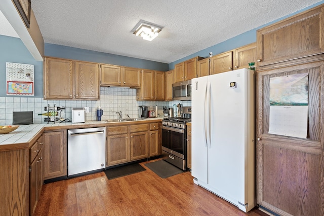 kitchen with tile countertops, wood finished floors, a sink, decorative backsplash, and stainless steel appliances