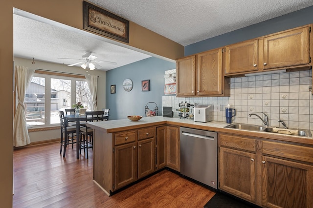 kitchen with a sink, tile countertops, dishwasher, a peninsula, and dark wood-style flooring