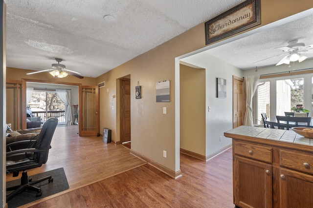 office area with visible vents, light wood-style flooring, a textured ceiling, and a ceiling fan