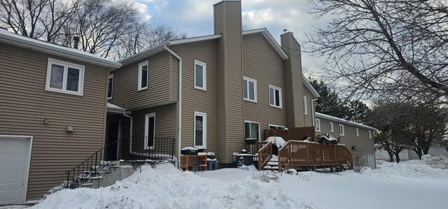 view of snow covered exterior with a deck, a chimney, and a garage