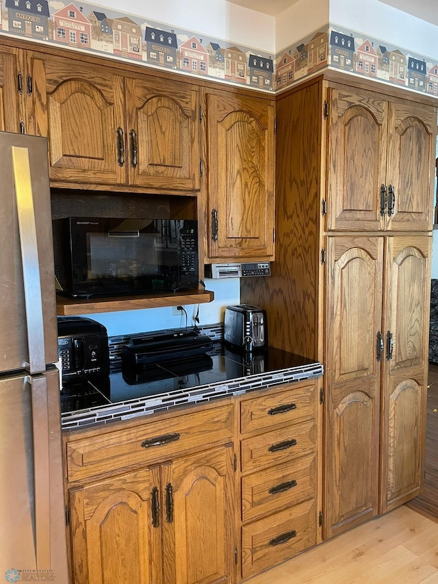 kitchen featuring freestanding refrigerator, light wood-style floors, brown cabinets, and black microwave