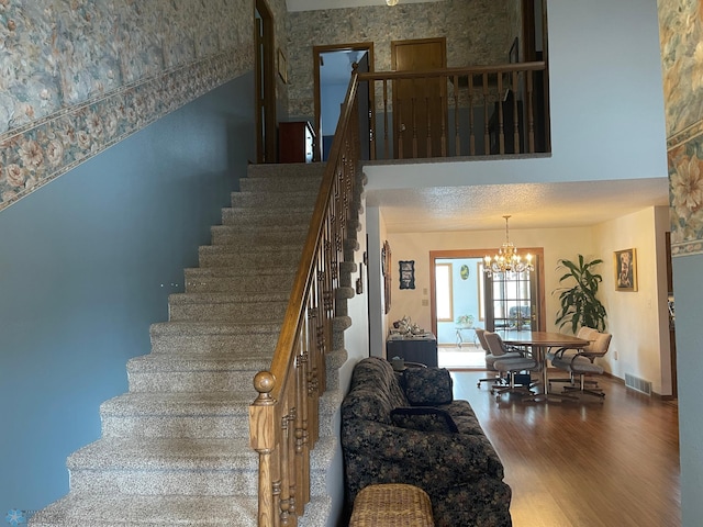 stairs featuring a textured ceiling, wood finished floors, visible vents, and a chandelier