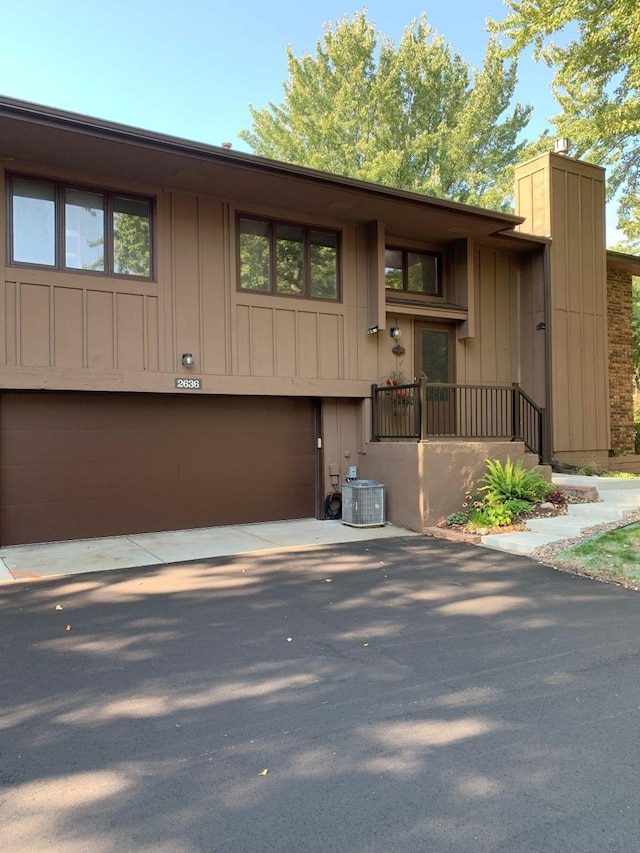 view of front of house with a chimney, central AC unit, board and batten siding, a garage, and driveway