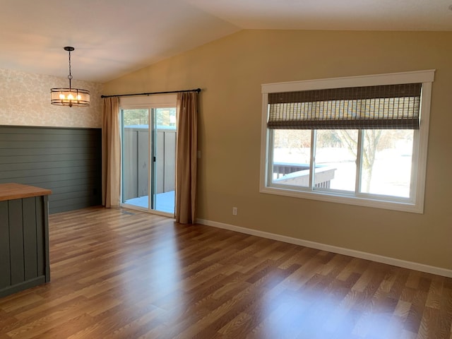 unfurnished dining area with lofted ceiling, a notable chandelier, baseboards, and wood finished floors