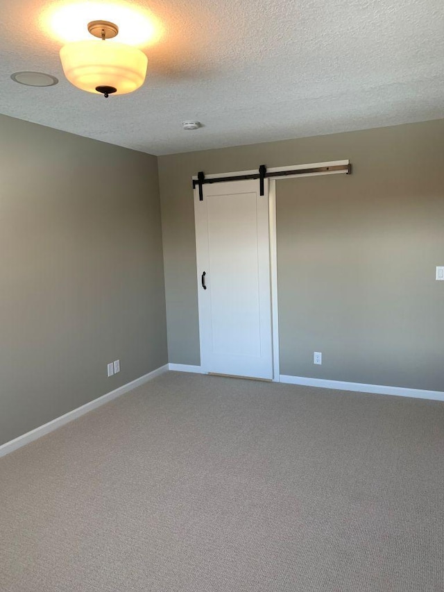 unfurnished room with light carpet, a barn door, a textured ceiling, and baseboards