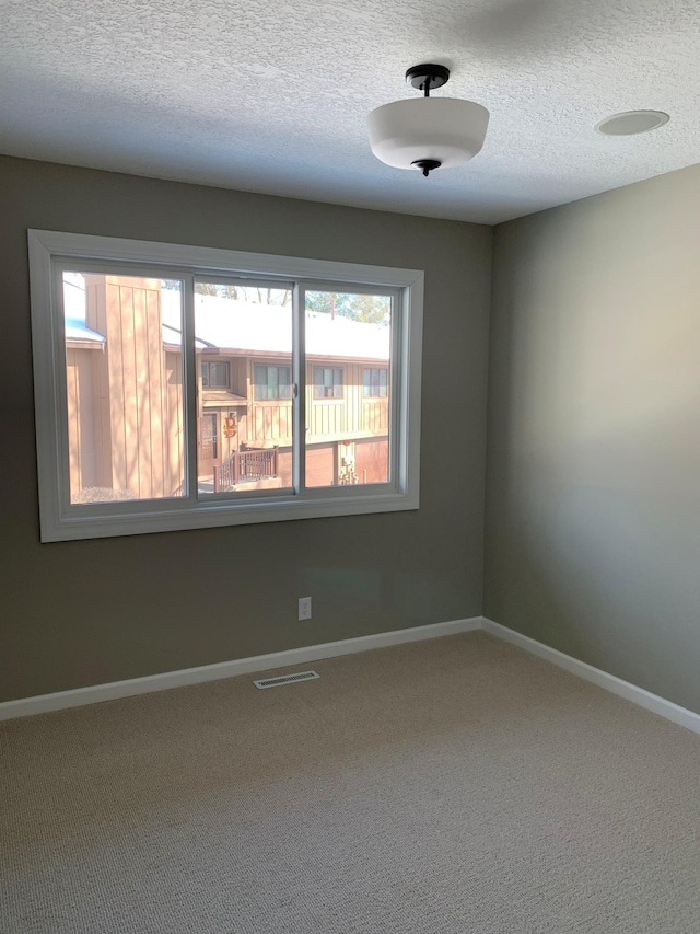 spare room with baseboards, a textured ceiling, visible vents, and carpet flooring