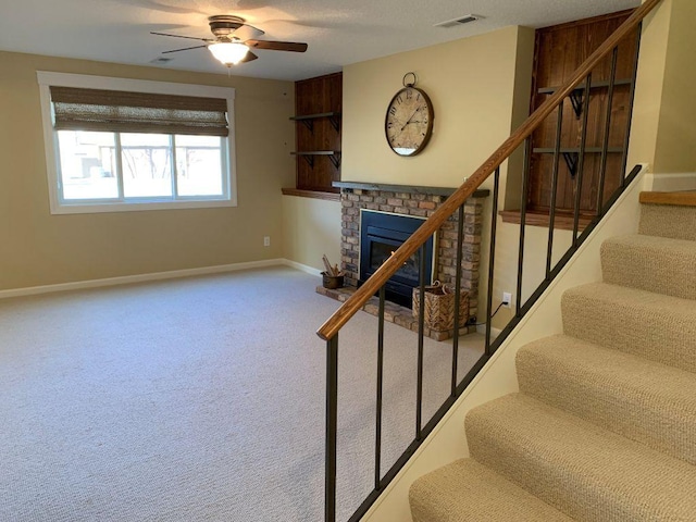 stairs featuring carpet floors, a ceiling fan, visible vents, baseboards, and a brick fireplace