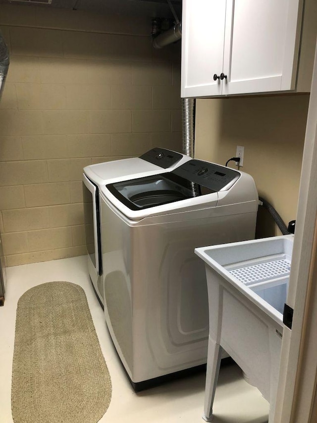 clothes washing area featuring concrete block wall, cabinet space, washer and clothes dryer, and a sink