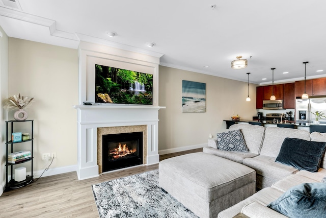 living area featuring visible vents, crown molding, baseboards, light wood-style flooring, and a glass covered fireplace