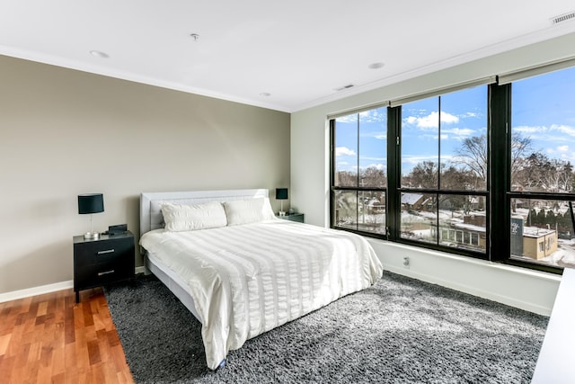 bedroom with visible vents, crown molding, baseboards, and wood finished floors