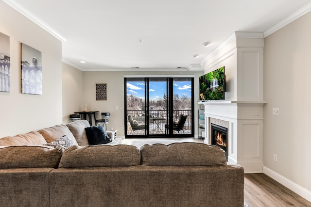 living room with a glass covered fireplace, baseboards, light wood-style floors, and ornamental molding