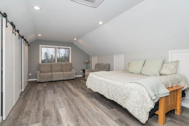 bedroom with a barn door, baseboards, visible vents, wood finished floors, and vaulted ceiling