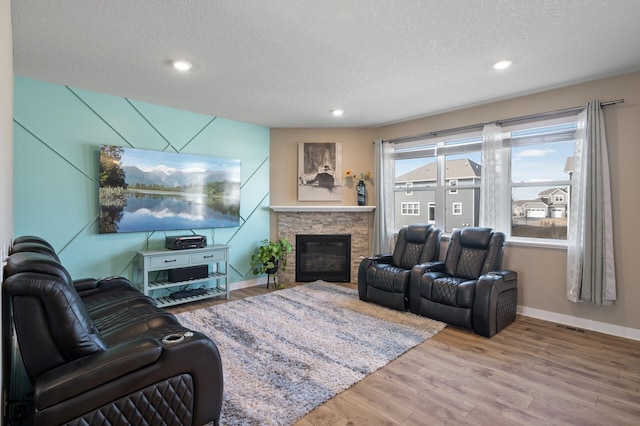 living area featuring a stone fireplace, wood finished floors, baseboards, and a textured ceiling