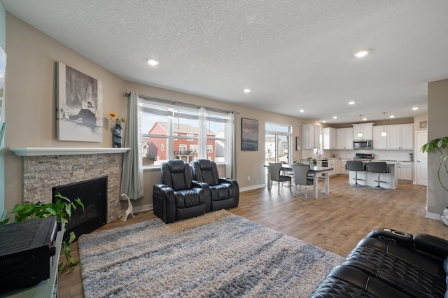 living area with baseboards, light wood-style flooring, recessed lighting, a stone fireplace, and a textured ceiling