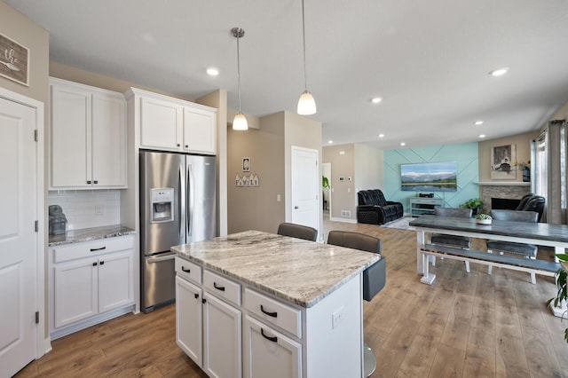 kitchen with a kitchen island, a fireplace, light wood-style floors, stainless steel refrigerator with ice dispenser, and open floor plan