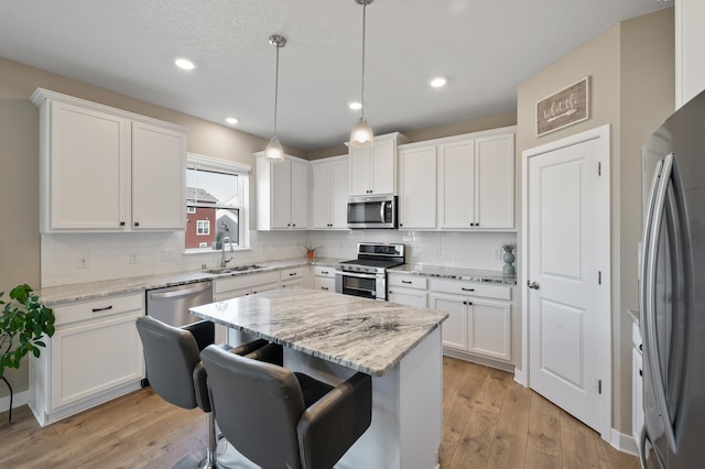 kitchen featuring a sink, a kitchen breakfast bar, white cabinetry, stainless steel appliances, and light wood finished floors