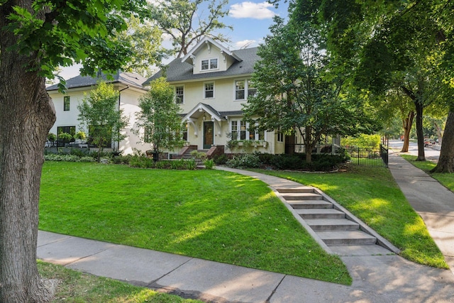 american foursquare style home featuring stucco siding, a front lawn, and fence