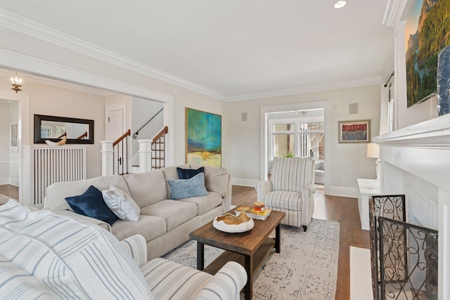 living area featuring a fireplace with flush hearth, wood finished floors, crown molding, baseboards, and stairs