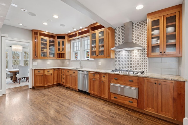 kitchen featuring a warming drawer, a sink, wood finished floors, appliances with stainless steel finishes, and wall chimney exhaust hood