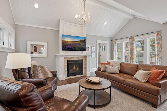 living area with wood finished floors, baseboards, lofted ceiling with beams, a glass covered fireplace, and a notable chandelier