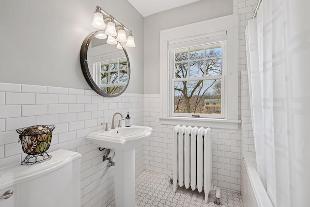 full bathroom featuring toilet, tile walls, radiator heating unit, and a healthy amount of sunlight