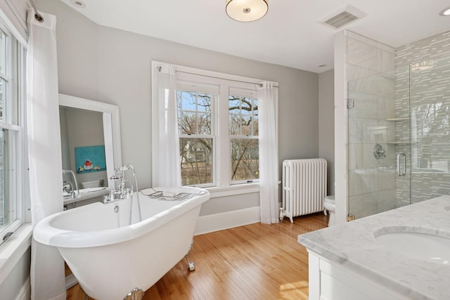 full bath featuring visible vents, radiator heating unit, a stall shower, a freestanding tub, and vanity