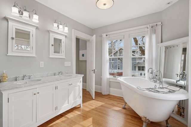 bathroom with a freestanding bath, wood finished floors, baseboards, and a sink