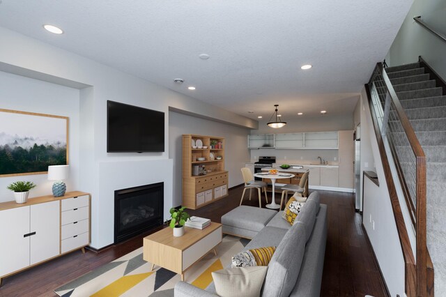 living area featuring stairs, a glass covered fireplace, dark wood finished floors, and recessed lighting