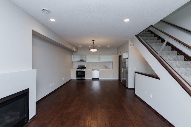 unfurnished living room featuring recessed lighting, visible vents, stairs, dark wood-style floors, and a glass covered fireplace