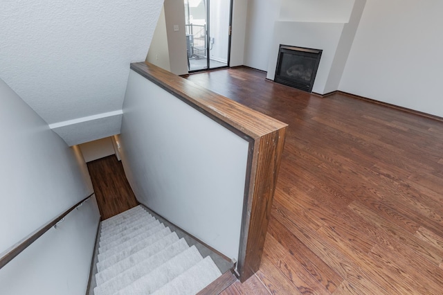 stairs with wood finished floors and a glass covered fireplace