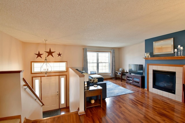 foyer with a tile fireplace, a textured ceiling, an inviting chandelier, and wood finished floors