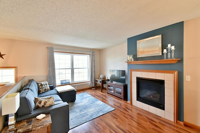 living area featuring baseboards, a textured ceiling, wood finished floors, and a tile fireplace