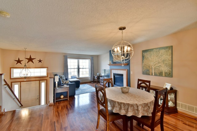 dining space with a tiled fireplace, visible vents, an inviting chandelier, and wood finished floors