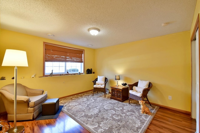 living area featuring a textured ceiling, baseboards, and wood finished floors