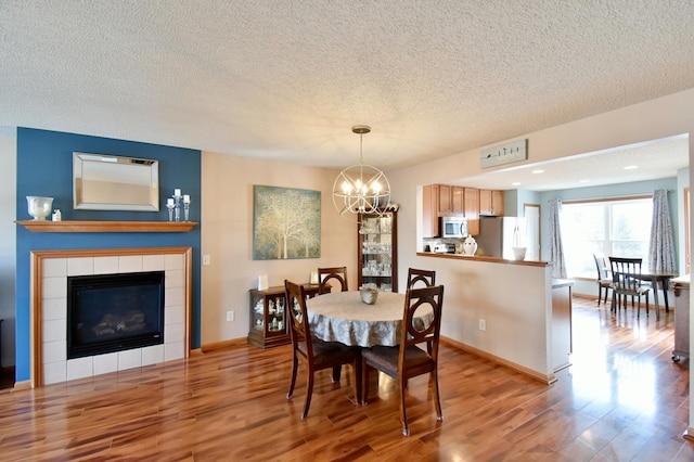 dining space with a chandelier, baseboards, wood finished floors, and a tile fireplace