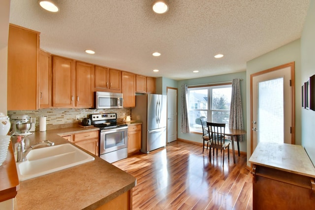 kitchen featuring light wood-type flooring, a sink, tasteful backsplash, recessed lighting, and stainless steel appliances