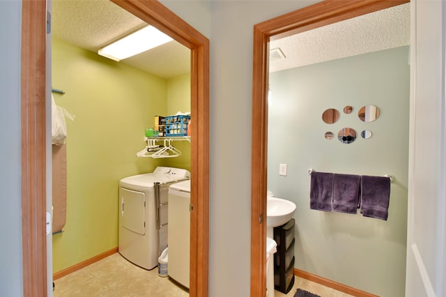 clothes washing area with baseboards, separate washer and dryer, laundry area, and a textured ceiling