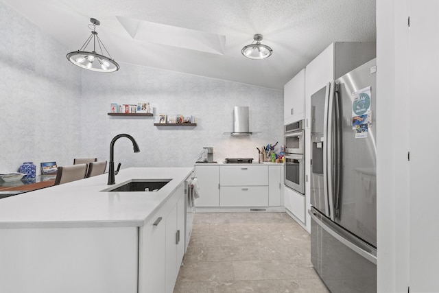 kitchen with light countertops, white cabinets, stainless steel appliances, wall chimney exhaust hood, and a sink