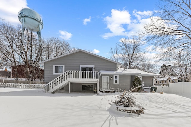 snow covered house featuring a deck, stairs, and fence