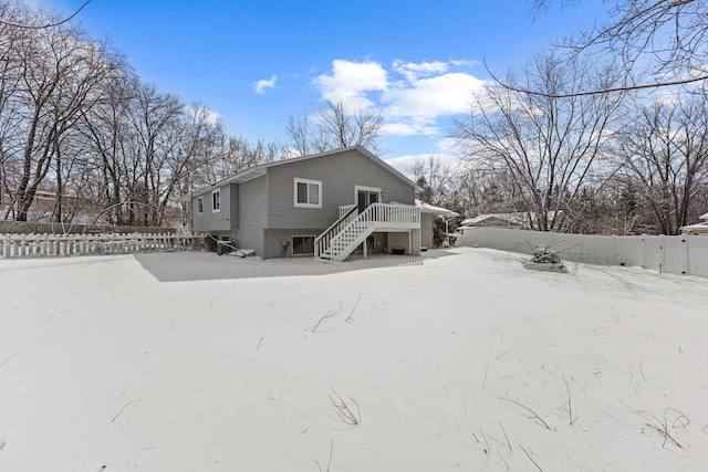 snow covered house featuring stairway, fence, and a wooden deck